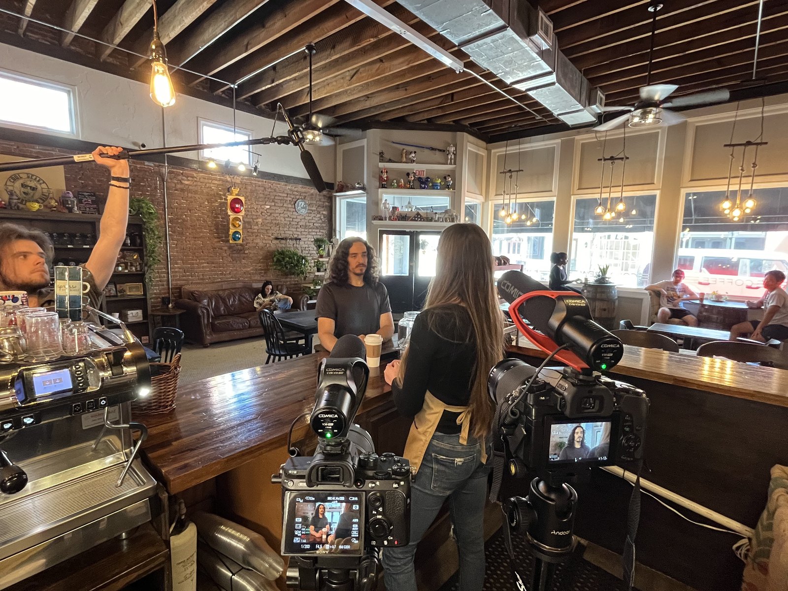 A two-camera setup with a boom mic on a coffee shop set